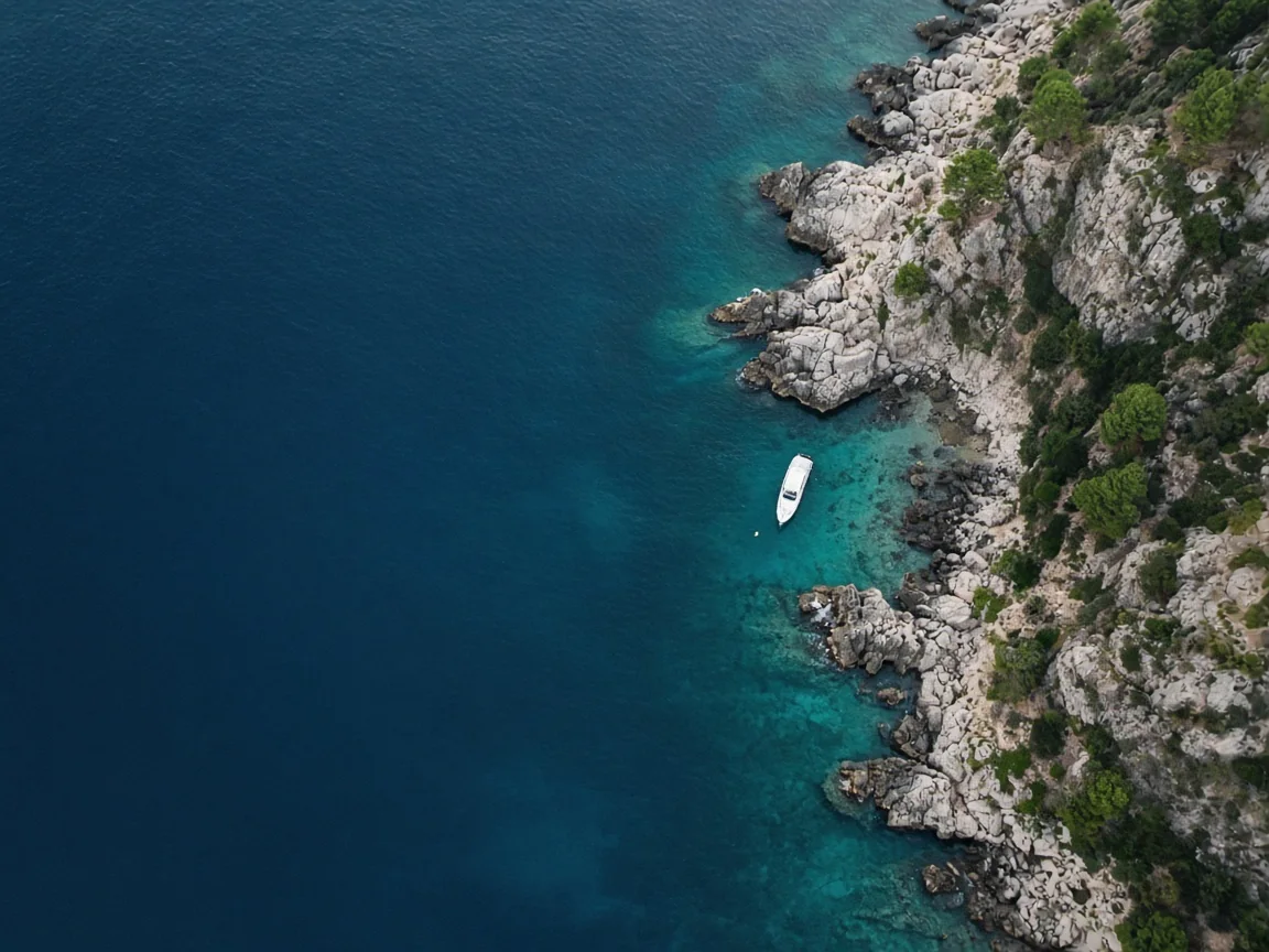 Aerial view of a yacht anchored in a turquoise cove along a rocky coastline